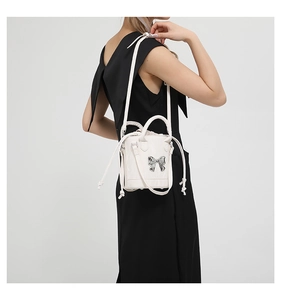 Detail of white bucket bag with silver bow accent and versatile crossbody shoulder strap