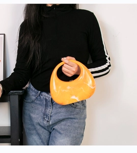 Detail of orange marble acrylic crescent clutch held by a model in black top and jeans