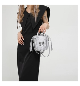 Detailed view of silver metallic bucket bag with bow ornament on black dress