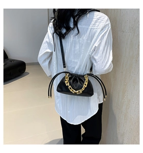 Detail of black lychee grain leather drawstring bag with thick gold chain handle on model