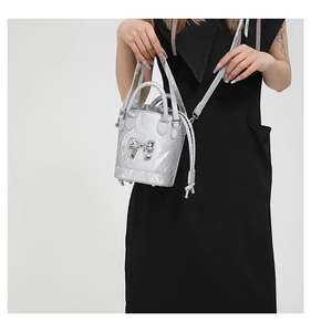 Detail of silver metallic bucket bag with ribbon bow and textured pleats on a model