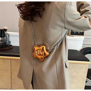 Detail of star-shaped bright orange crossbody bag with chain strap on a model