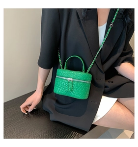 Dettaglio mini borsa vanity verde con tracolla a catena su un blazer nero