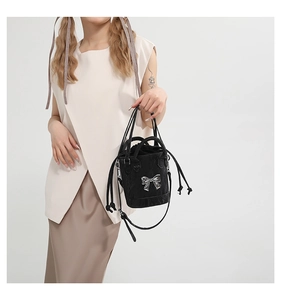 Detail of black pleated leather bucket bag featuring a silver metal bow and drawstring