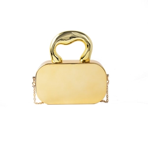 Golden hard shell clutch bag with large metallic handle and chain shoulder strap