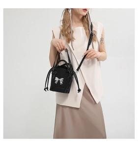 Detail of a black bucket bag with a silver metal bow and drawstring closure