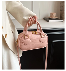 Detail of pink faux crocodile leather handbag featuring heart-shaped accents and double zippers