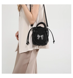 Detail of black mini bucket bag with glossy finish and silver bow accent