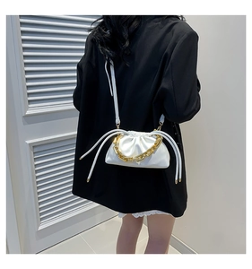 Close-up of a white cloud bucket bag with chunky gold chain detail on a black blazer