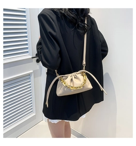 Detail of beige drawstring bucket bag with thick gold chain handle and leather texture