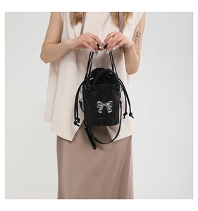 Detail of black drawstring bucket bag featuring a metallic silver bow and pleated texture
