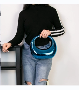 Close-up of a glossy metallic blue dumpling crossbody bag styled on a female model