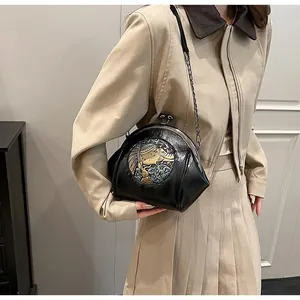 Detail of vintage black shell bag with retro metal relief and chain strap on model