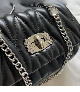 Detail of silver rhinestone-embellished turn-lock on black quilted leather crossbody bag
