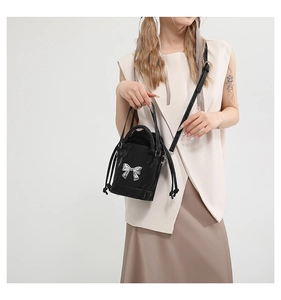 Detail of black mini bucket bag with silver metal bow and adjustable shoulder strap