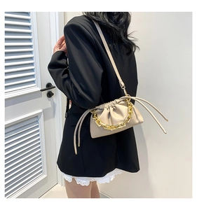 Detail of beige pleated cloud bag with chunky gold chain strap worn by a model