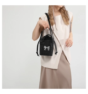Detail of black bucket bag featuring a large silver bow and elegant drawstring closure