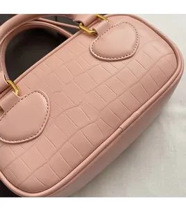 Detail of pink crocodile embossed leather handbag with golden hardware and neat stitching