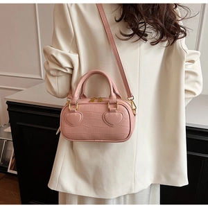 Detail of pink croc-effect mini bag featuring 3D heart patches and gold zippers