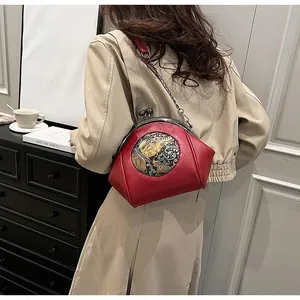 Detail of red leather shell bag with ethnic elephant embroidery and metal chain strap