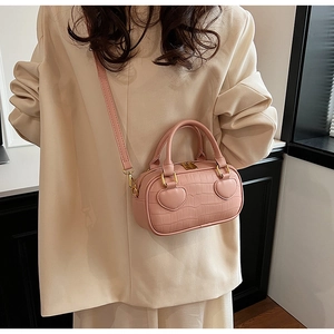 Detail view of pink crocodile textured handbag with heart accents on beige blazer