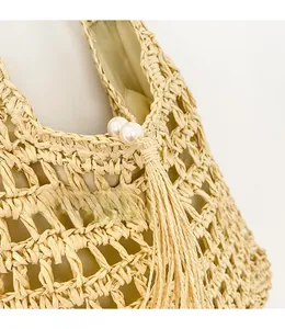 Detail of straw tote bag featuring elegant pearl closure and long tassels decoration