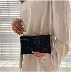Detail of a black glossy textured box clutch bag with elegant golden chain strap