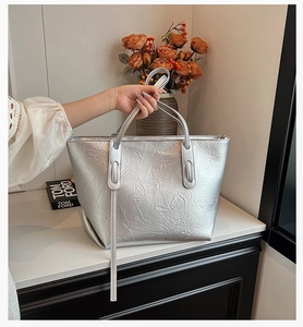 Detail of silver tote bag showing glossy metallic crinkled texture and slim handles