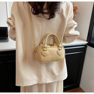 Detail of a chic cream handbag featuring crocodile pattern and gold hardware on a model