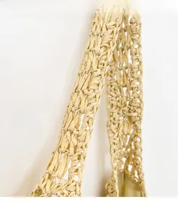 Detail of hollow-out straw tote bag showing the wide shoulder strap and woven texture
