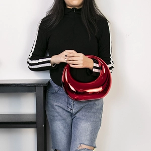 Chic red patent leather crescent crossbody bag shown in a stylish model handheld pose