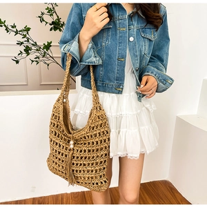 Detailed shot of hollow woven straw tote bag featuring white pearl and long tassel accents