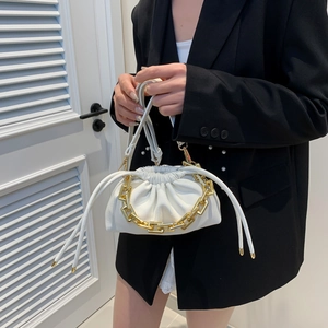 White ruched cloud bucket bag with bold gold chain strap shown on a black suit blazer