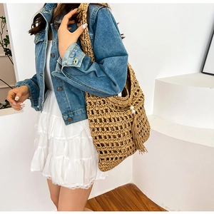 Detail of hollow-out straw tote bag with fringe and pearl accents on casual model