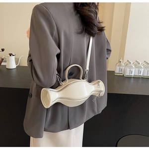 Sac à main blanc en cuir en forme de nœud porté en bandoulière sur une veste grise