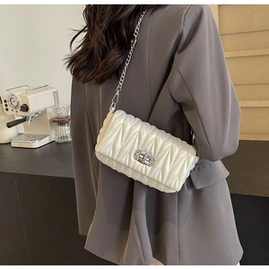 Detail of white quilted crossbody bag with crystal lock shown on shoulder