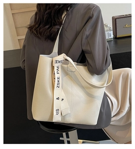 Detail of a beige pebbled leather tote bag with a decorative ZSKE PARIS printed ribbon