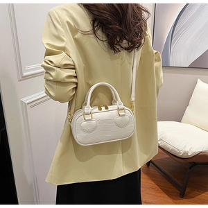 Detail of white crocodile embossed crossbody bag with heart patches and gold hardware