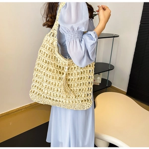Detail view of beige hollow woven straw tote bag with tassel and pearl charms for summer
