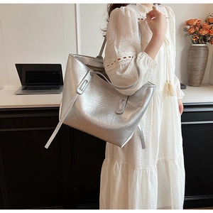 Detail view of large silver tote bag with crinkled texture on a shoulder strap model