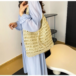 Detail of hollow woven straw tote bag featuring elegant pearl and long tassel charms