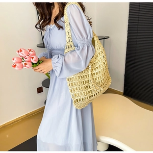 Detailed close-up of beige woven straw tote bag featuring hollow texture and pearl tassel