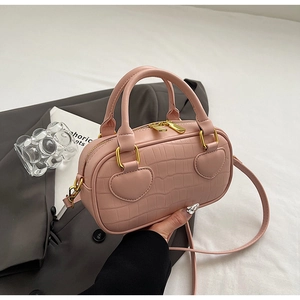 Detail of pink crocodile embossed handbag with golden heart-shaped hardware and fine stitching