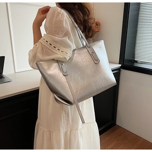Detail of large silver tote bag showing crinkled texture and long shoulder strap on model