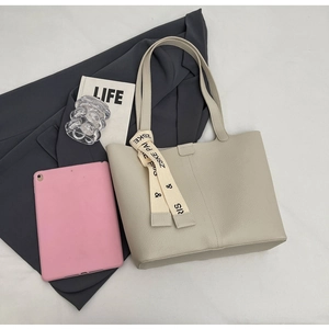 Detail of beige tote bag with litchi grain texture and a decorative printed silk scarf