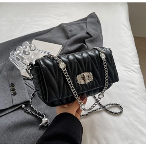 Macro detail of wave quilted black leather with crystal-embellished silver lock and chain