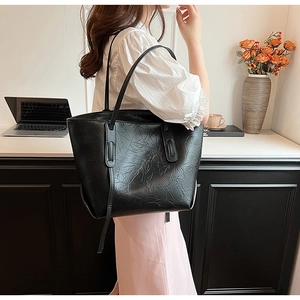 Detail of a large black tote bag featuring wrinkled faux leather texture and slender straps