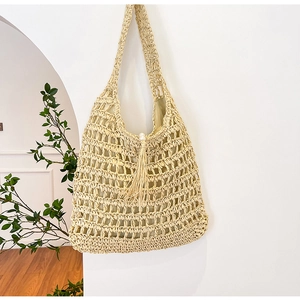 Close-up of woven hollow-out straw tote bag with delicate tassels and pearl detail