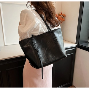 Detail of a large black tote bag with wrinkled oil wax texture and long decorative straps