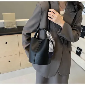 Détail du sac seau en cuir noir grainé avec foulard géométrique en soie et bandoulière